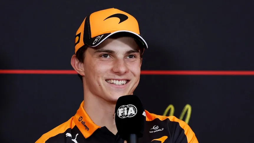 Oscar Piastri holding a microphone and smiling during a media conference